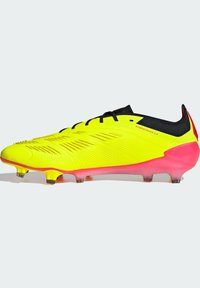 Scarpa da calcio gialla con tomaia texturizzata, dettagli neri e suola rosa. Caratterizzata da numerosi tacchetti per la trazione e un design a taglio basso.