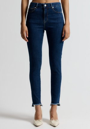 High-waisted dark blue skinny jeans with frayed hem, featuring front pockets and a zipper fly. Made of denim with a smooth texture.