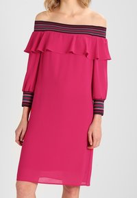 Vestido fucsia off-the-shoulder con escote con volantes, que presenta acentos a rayas en azul marino y burdeos en las mangas. Textura sedosa, corte recto.