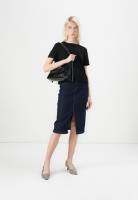 T-shirt noir à manches courtes, jupe crayon en denim foncé avec fente à l'avant, talons beiges et sac à main noir avec bandoulière.