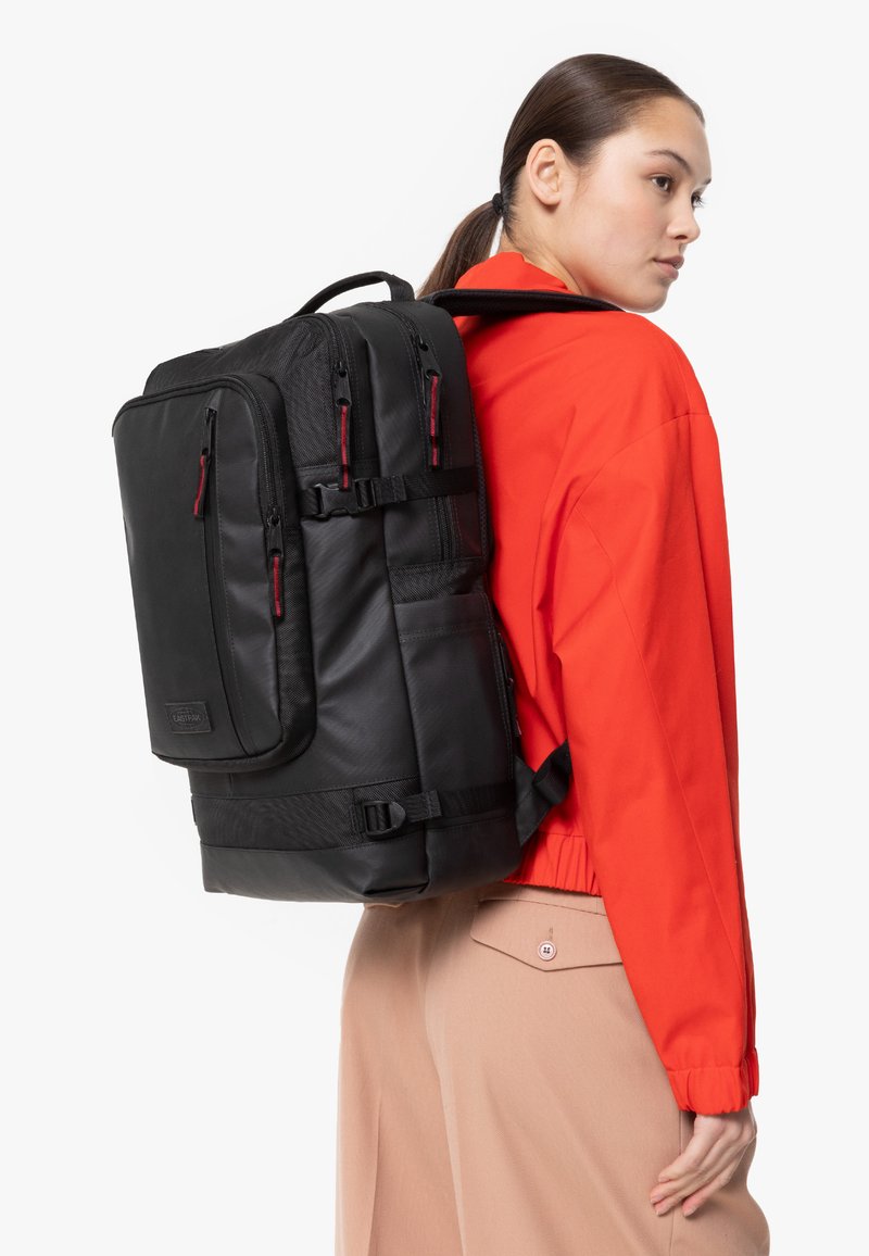 Svart ryggsäck med flera dragkedjefickor, justerbara remmar och en strukturerad yta. Utrustad med röda dragkedjor som accent och en stabil bas.