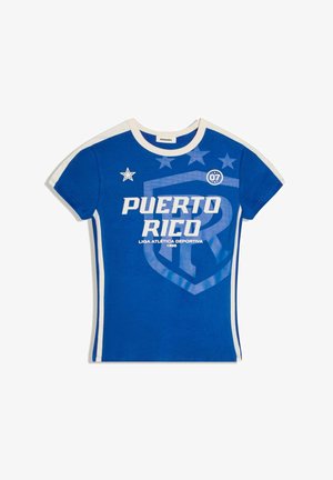 Kék rövid ujjú póló fehér szegéllyel, fehér "Puerto Rico" felirattal, csillagokkal és sport pajzs logóval az elején.