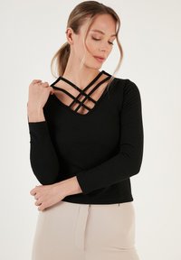Maglietta nera a maniche lunghe con scollatura a V e dettagli incrociati sulla scollatura, caratterizzata da una silhouette aderente e una texture morbida.
