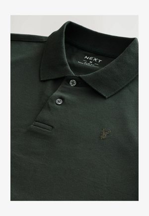 Tamsiai žalia polo marškinėliai su įribuotu apykakle, trimis mygtukais ir mažu siuvinėtu elnio logotipu kairėje krūtinės pusėje.