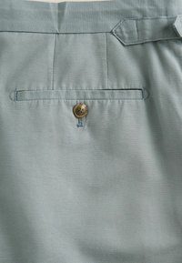 Helle blaue Baumwollshorts mit einer Gesäßtasche mit einem runden goldenen Knopf, feiner diagonaler Textur und Gürtelschlaufen am Bund.