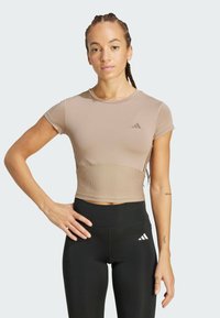 Top atlético corto en color topo con mangas cortas, textura acanalada en la cintura y un logo sutil. Combinado con leggins negros de talle alto.