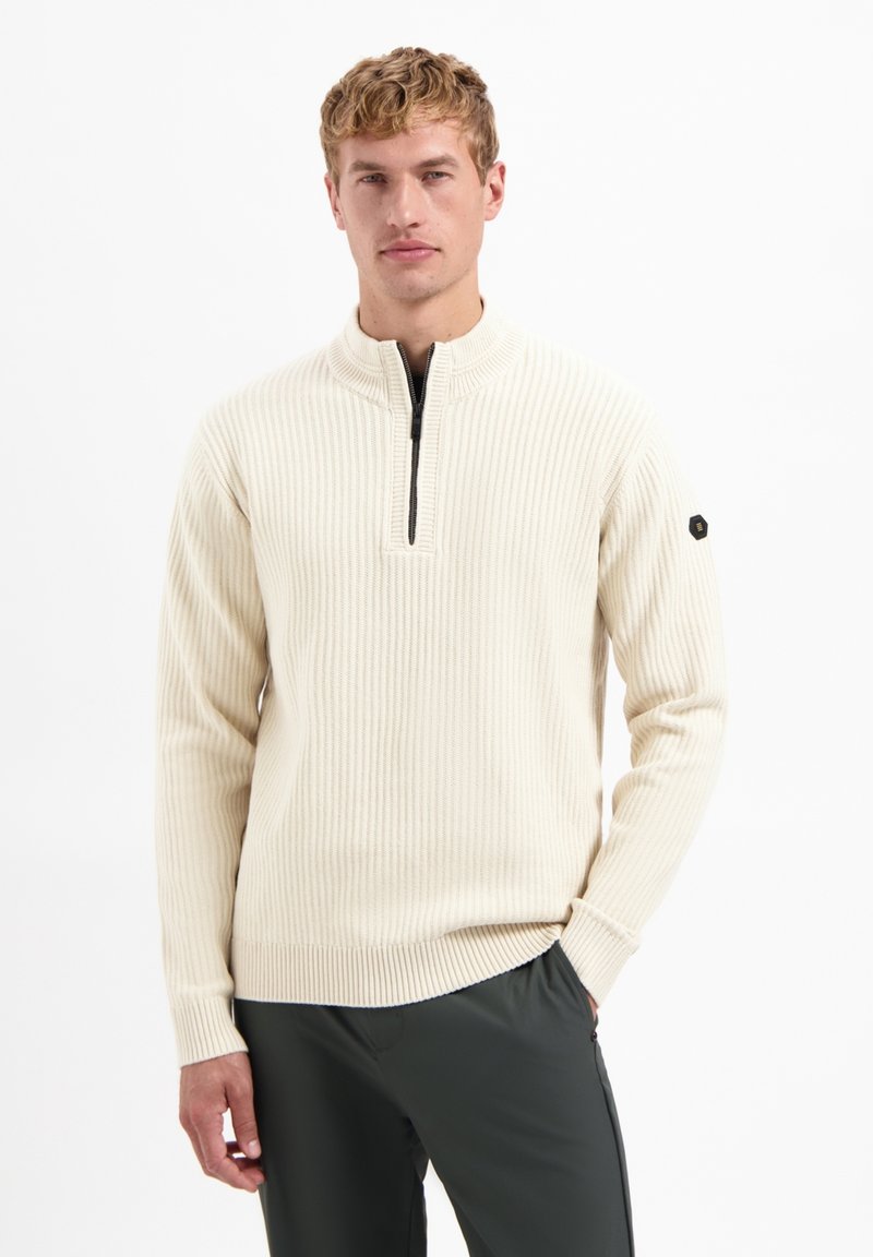 Ivory ribbed pullover with a half-zip collar, featuring long sleeves and a black logo accent on the left sleeve. Soft knit texture.