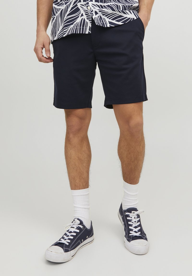 Shorts bleu marine en tissu coton mélangé, avec une coupe droite et des poches latérales, associés à des chaussettes blanches et des baskets sombres.