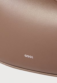 Λείο καφέ δερμάτινο επιφάνεια με μικρό λευκό λογότυπο "OSOI" ανάγλυφο κοντά στην κάτω άκρη.