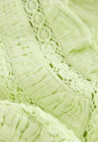Tissu vert clair doux avec des motifs de maille texturée alternés et des détails en dentelle ouverte, présenté en gros plan avec des plis.