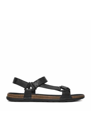 Schwarze flache Sandale mit verstellbaren Riemen und korkstrukturierter Innensohle auf einer schwarzen Gummisohle, seitlich betrachtet.