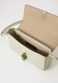 Structured, light green leather handbag with gold hardware, featuring a detachable strap and interior zip pocket. Smooth exterior texture.