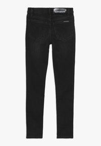 Pantalones ajustados de mezclilla negra con una cintura de altura media, que cuentan con dos bolsillos traseros y una etiqueta de Calvin Klein Jeans encima de la cintura.