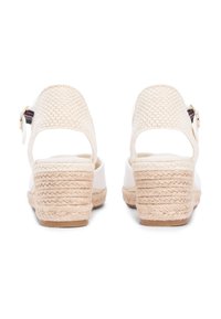 Compensées espadrilles blanches avec talon en jute tressé, dos ouvert et détail de boucle en métal. Tige lisse avec talon texturé, semelle plate.