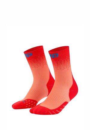 Paar rote und korallenfarbene Sportsocken mit Farbverlauf, blauer Beschriftung am Bündchen und strukturierten Sohlen, auf weißem Hintergrund aufrecht dargestellt.