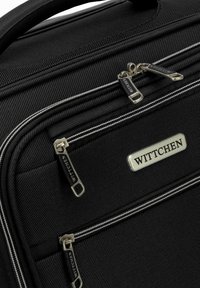 Černý kufr vyrobený z texturované tkaniny s třemi stříbrnými zipy, označenými táhly a kovovou destičkou s logem se jménem "WITTCHEN."