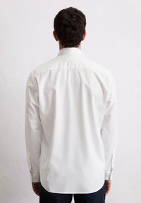 Witte lange mouw overhemd met kraag, voorzien van een gladde textuur en knoopmanchetten, gezien van achteren, met een gebogen zoom.