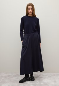 Navy Pullover mit langen Ärmeln, kombiniert mit einem fließenden navyblauen Maxikleid mit elastischem Bund. Getragen mit schwarzen klobigen Loafers.