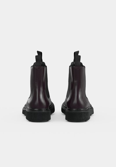Paire de bottines en cuir noir avec languettes et semelles épaisses nervurées, vues de dos sur un fond clair uni.