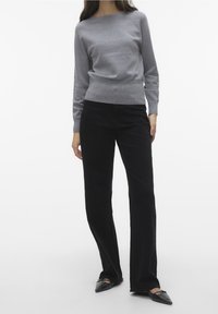 Szary sweter z dzianiny z okrągłym dekoltem, zestawiony z czarnymi rozszerzanymi spodniami i czarnymi czółenkami na płaskim obcasie, na jednolitym tle.