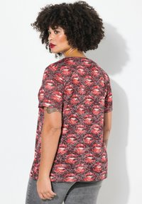 Camisa de manga corta con un patrón en rojo y negro que presenta labios; cuello redondo; tejido suave con un acabado ligeramente texturizado; corte relajado.