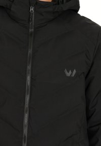 Svart isolerad jacka med dragkedjestängning och huva. Har en matt svart logotyp på bröstet och textil med struktur.