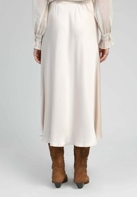 Jupe midi en satin beige clair avec une texture lisse, dotée d'une taille élastique et d'une légère évasement au bas, associée à des bottes de cowboy marron.