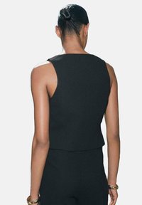 Schwarzes ärmelloses Crop-Top mit einem klaren Design, maßgeschneidertem Schnitt und glatter Textur, von hinten gesehen. Subtile Nahtdetails am Saum.