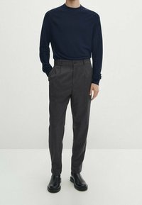 Laivastonsininen pitkähiha paita, harmaat räätälöidyt korkeavyötäröiset housut ja mustat nilkkurit. Sileät materiaalit ja klassinen muotoilu, minimalistinen tyyli.