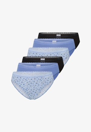 Mujer sonriente con un sostén azul y ropa interior de patrón azul claro, con un brazo levantado detrás de la cabeza, sobre un fondo blanco liso.