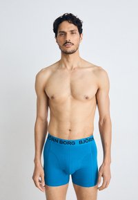 Blue men’s boxer briefs with a black "BJÖRN BORG" logo waistband. Fabric appears smooth with a fitted design and mid-length cut.
