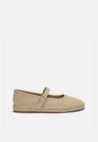 Beige Wildlederschuh mit runder Zehenpartie, Knöchelriemen und metallischem Schnallenverschluss. Verfügt über auffällige Nietenverzierungen und eine geflochtene Jute-Sohle.