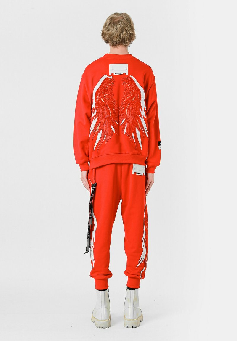 Conjunto de sudadera roja y pantalones con grandes gráficos de alas blancas en la parte posterior, con acentos blancos contrastantes y costuras detalladas.