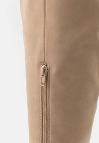 Béžová kozačka sahající po kolena s hladkou semišovou texturou, vybavená bočním světle zbarveným zipem pro snadné obouvání.