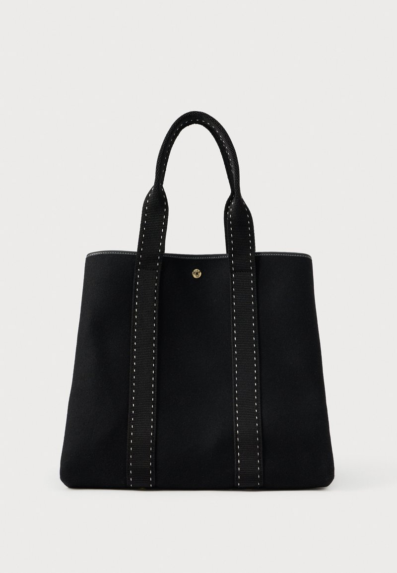 Μαύρη τσάντα tote με δύο δομημένες λαβές, που διαθέτει αντίθετη λευκή ραφή και στρογγυλό μεταλλικό λογότυπο στο μπροστινό μέρος.
