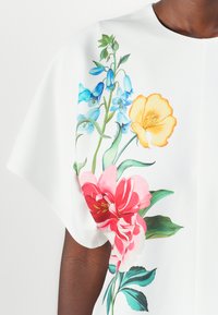 White garment featuring vibrant floral print, including pink, yellow, and blue flowers with green leaves, crafted from smooth fabric.