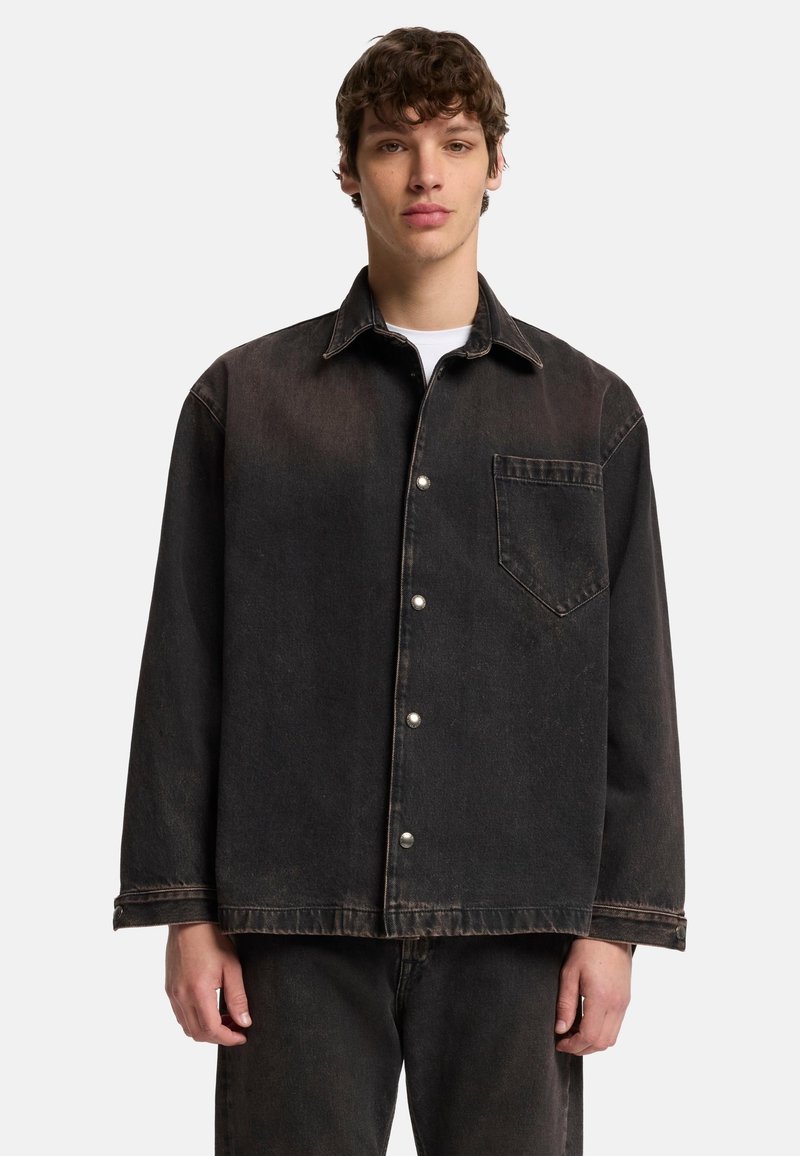 Veste en denim noire avec une coupe ample, dotée d'un col pointu, d'une poche avant et d'une fermeture à boutons-pression. Texture usée avec un léger délavage.