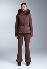 Jakna s prošivima i remenom, s umjetnim krznom na ovratniku, tamnoljubičaste boje, u paru s odgovarajućim širokim hlačama. Materijal izgleda glatko i rastezljivo.