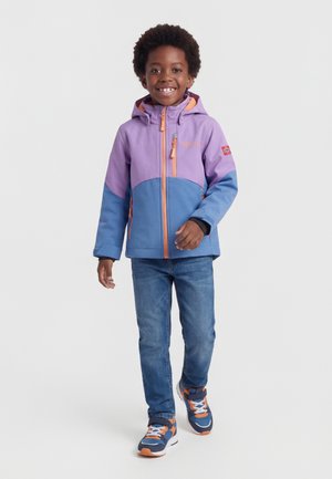 Χαμογελαστό παιδί που περπατάει προς τα εμπρός φορώντας μωβ και μπλε μπουφάν με κουκούλα, μπλε τζιν και πορτοκαλί και μπλε αθλητικά παπούτσια σε λευκό φόντο.