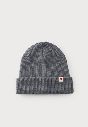 Bonnet gris tricoté avec revers plié et petite étiquette de logo rouge et blanc sur le revers, posé à plat sur fond blanc.
