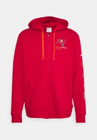 Rød zip-up hættetrøje lavet af blødt stof. Har orange snore og Tampa Bay Buccaneers logo på brystet, med yderligere grafik på ærmerne.