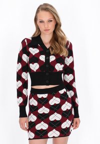 Strihnutá súprava kardigana a sukne v burgundskej, čiernej a bielej farbe. Obsahuje srdiečkové vzory a čierne gombíky; pletená látka s rebrovanými detailmi.