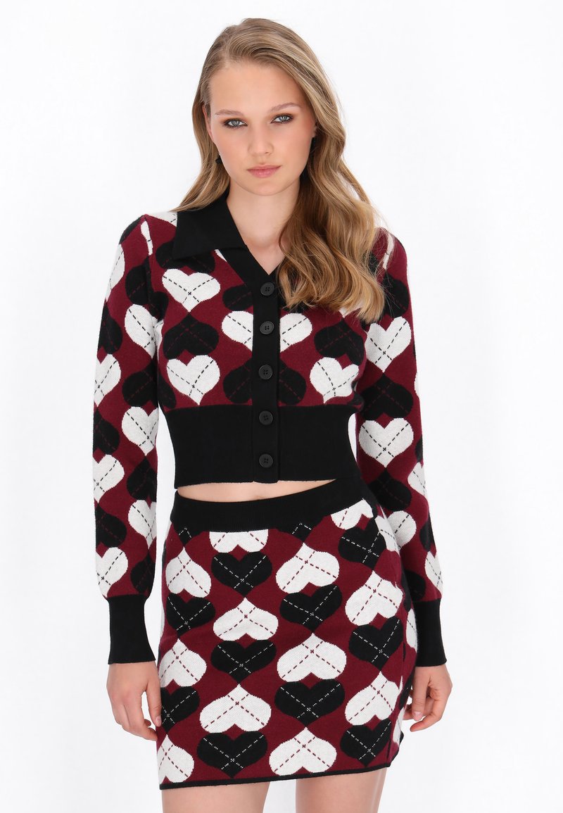 Strihnutá súprava kardigana a sukne v burgundskej, čiernej a bielej farbe. Obsahuje srdiečkové vzory a čierne gombíky; pletená látka s rebrovanými detailmi.