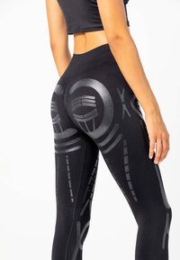 Zwarte legging met reflecterende geometrische patronen, hoge tailleband en rekbare stof voor comfort en bewegingsvrijheid.