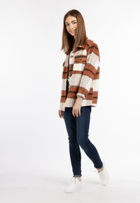 Bruine en witte geruite jas met knopen, gemaakt van een textuurstof, gecombineerd met donkere skinny jeans en witte sneakers.