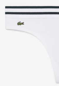 Culotte blanche côtelée avec double bande verte sur la ceinture élastique et logo crocodile vert brodé sur le côté gauche.