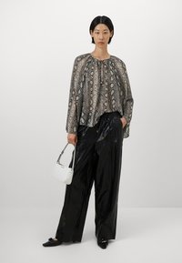 Vloeiende blouse met slangenprint en geplooide halslijn, gecombineerd met hoog-gecombineerde, glanzende zwarte wijde broek. Geaccentueerd met een kleine witte handtas.