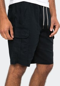 Black cargo shorts made of textured fabric, featuring side pockets, an elastic waistband with drawstrings, and subtle stitching details.