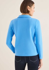 Lyseblå langærmet polo med krave, glat tekstur og lige snit, kombineret med mørke jeans med lyse syninger.