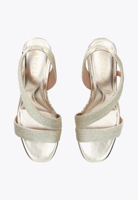 Gold sandals featuring a metallic finish, with textured fabric straps crossing over the foot. Pink inner lining. Open-toe design.